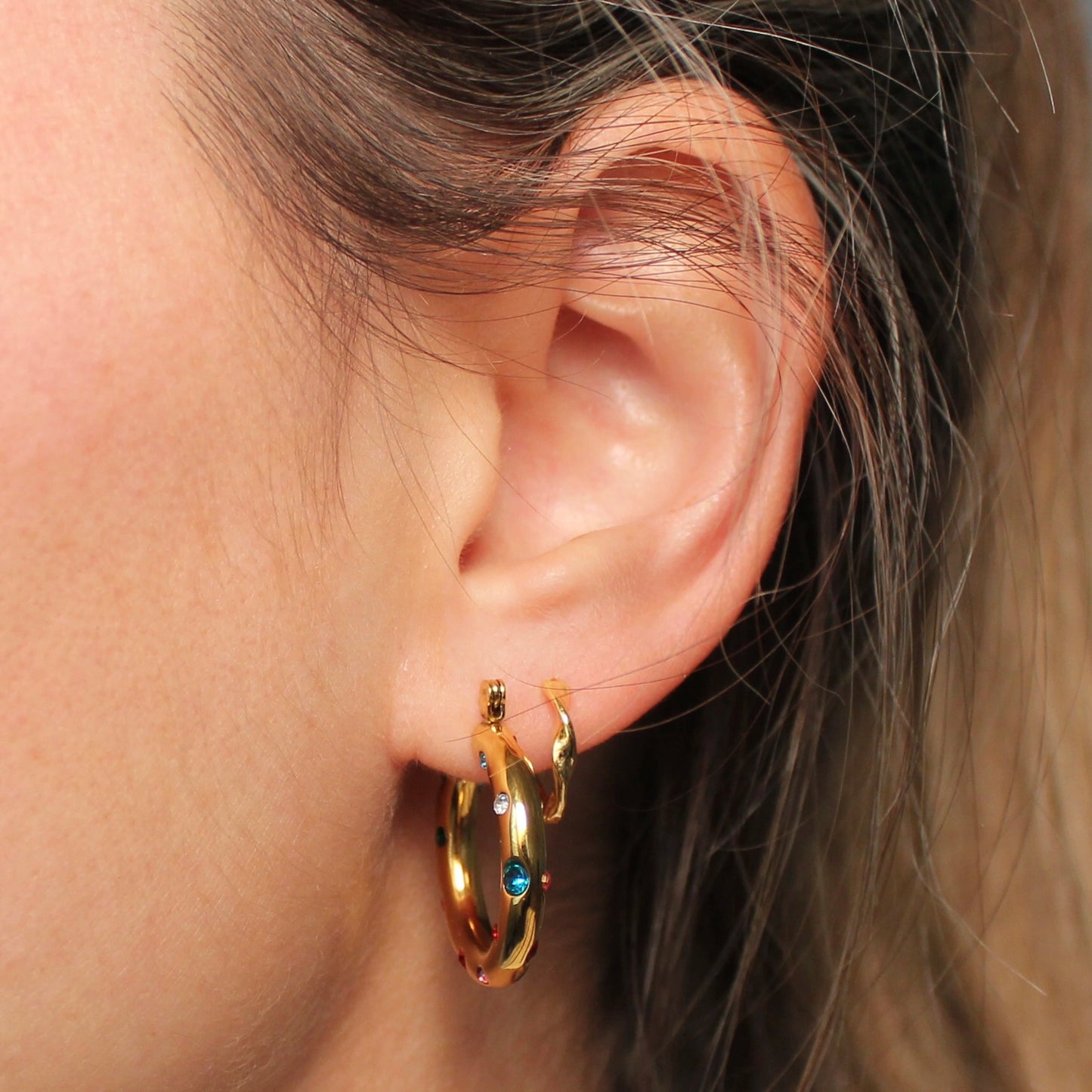 Gouden hoops met gekleurde steentjes in een oor