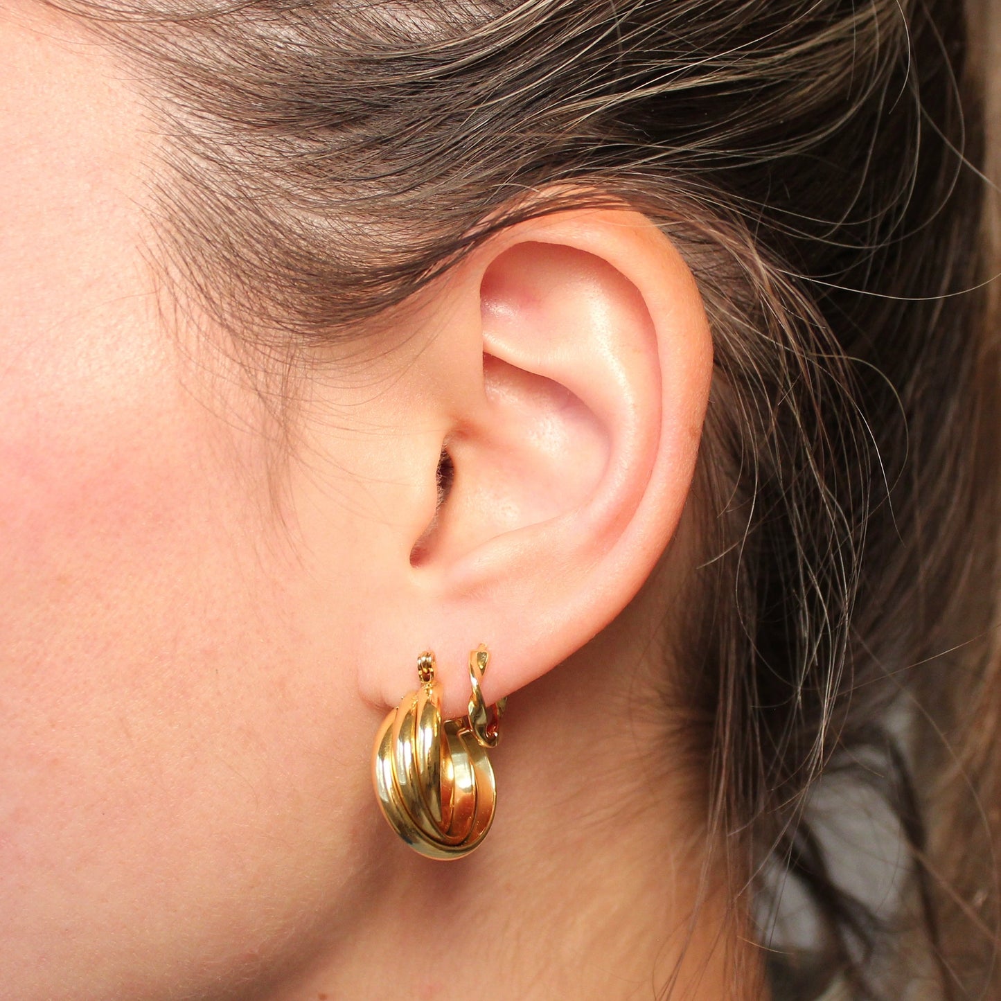 Twee gouden hoops in een oor waarvan er een bestaat uit drie gedraaide ringen