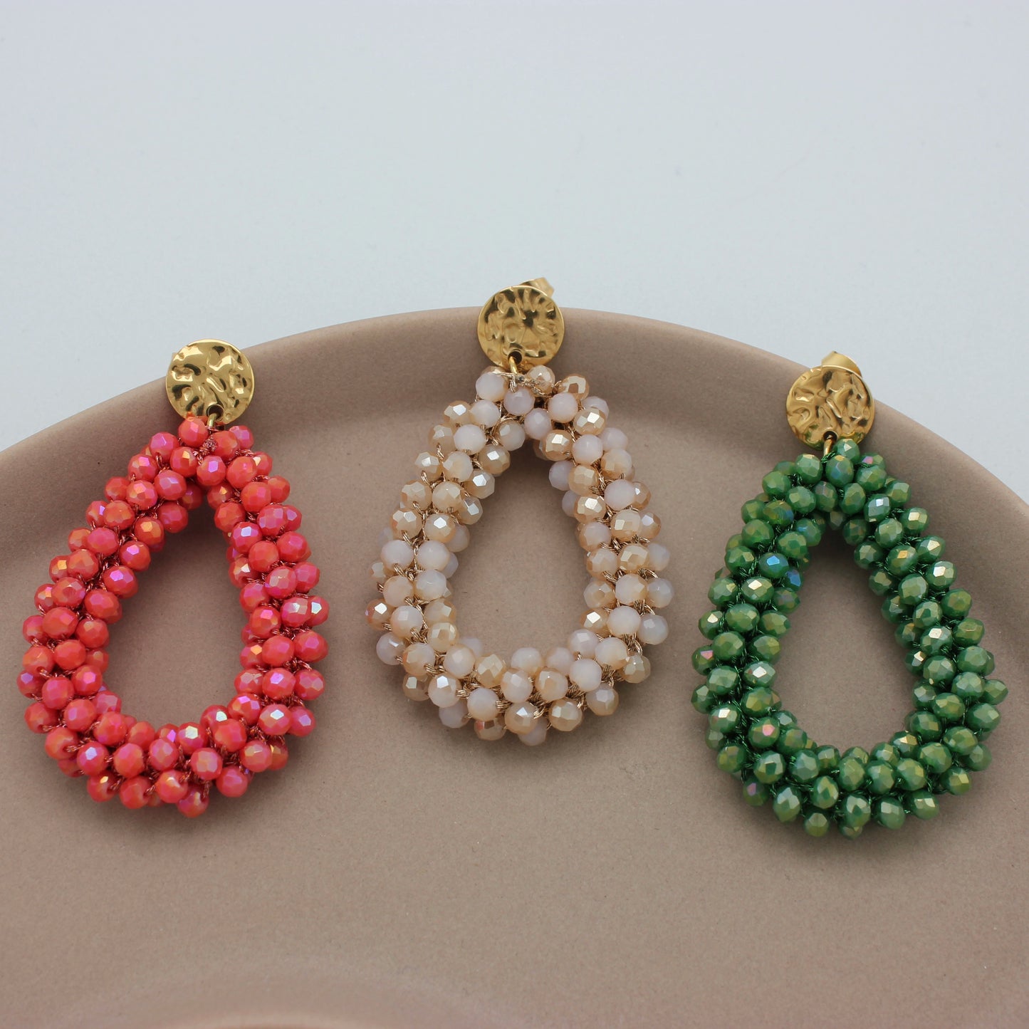 Drie gouden oorbellen met groene, beige en koraal kleurige kristallen kralen