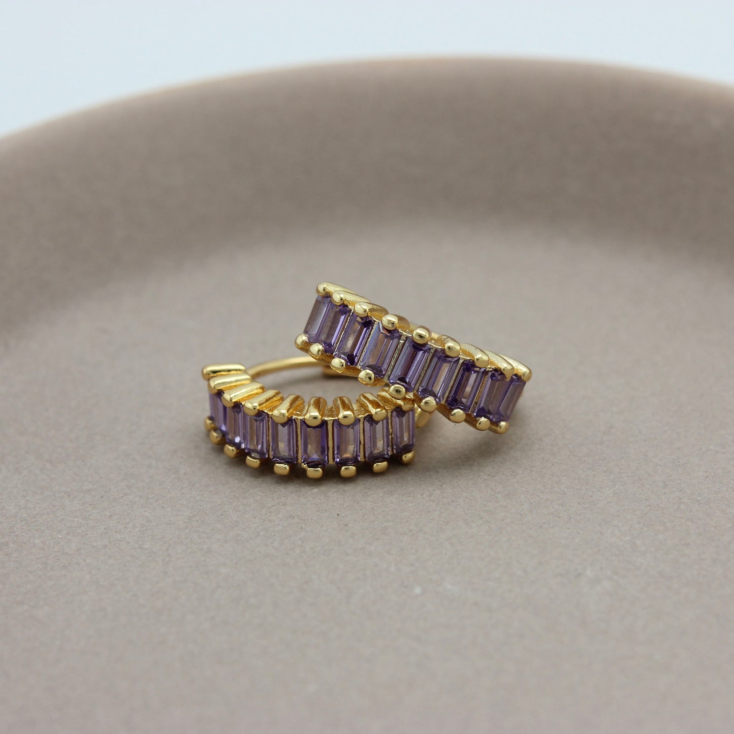 Gouden hoops met paarse zirkonia steentjes liggend op een schaaltje