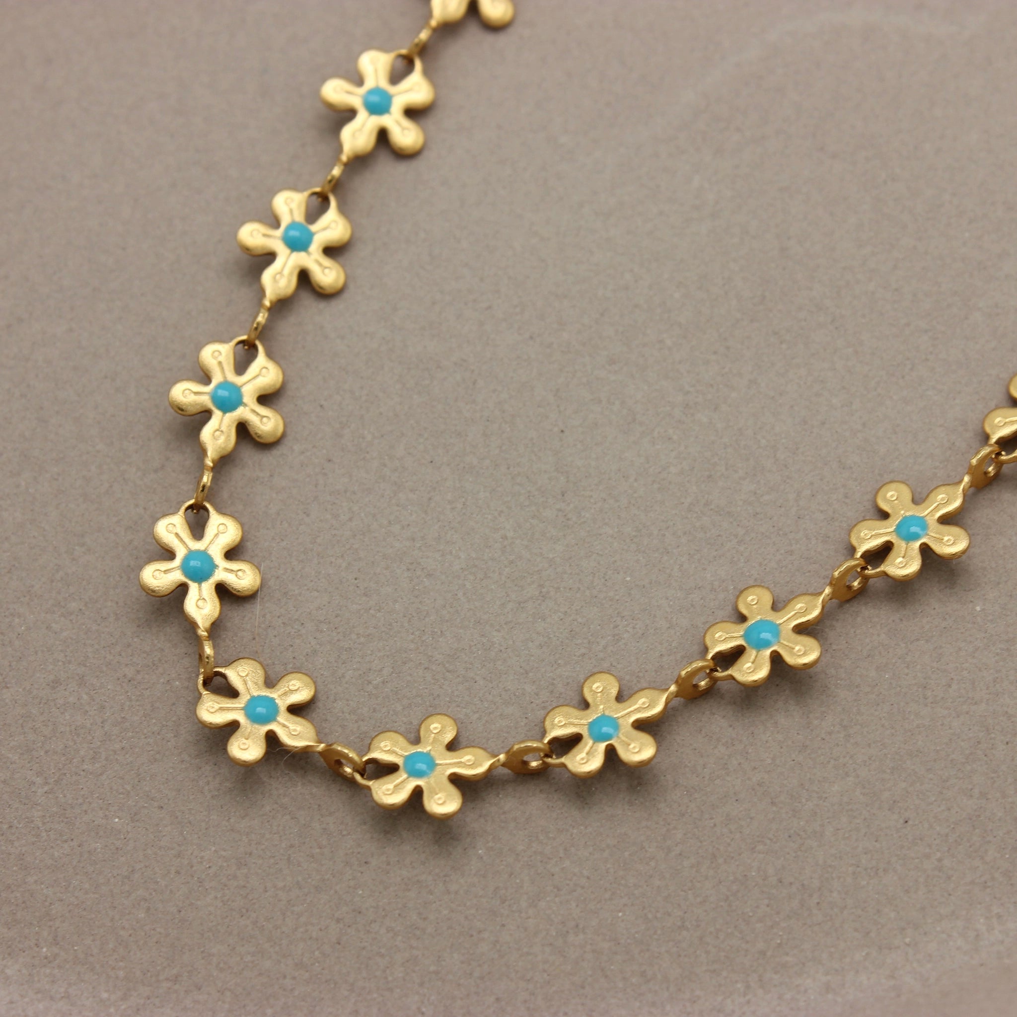 Gedetailleerde foto van een gouden bloemen ketting met een blauwe stip