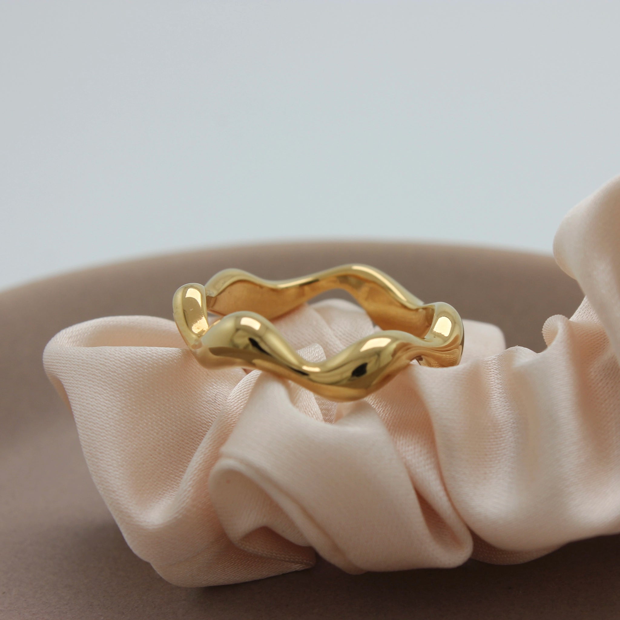 Een Asymmetrische gouden Ring Abby op een stuk stof