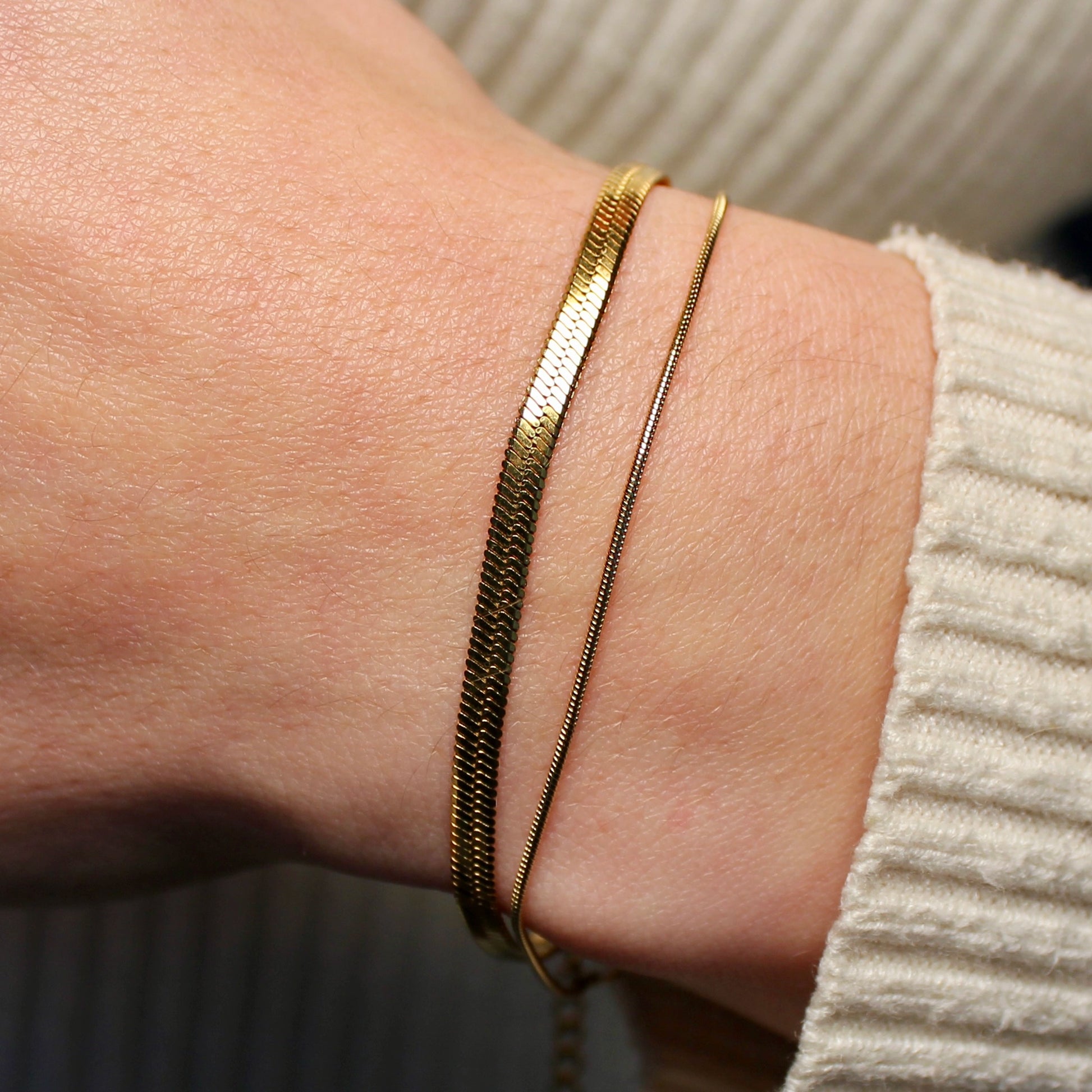Een platte gouden snake armband en een ronde snake armband om een pols