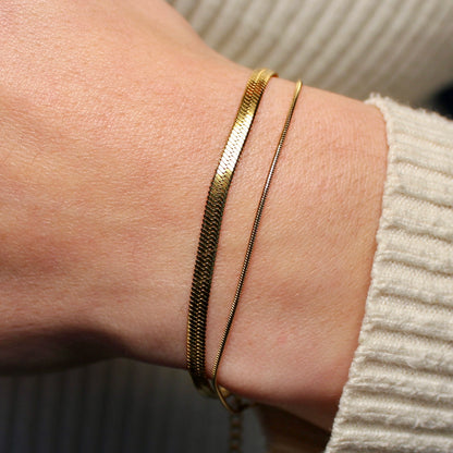 Een platte gouden snake armband en een ronde snake armband om een pols