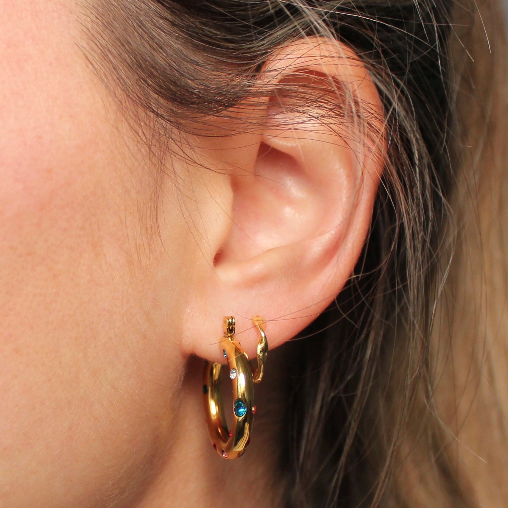Gouden hoops met gekleurde steentjes in een oor