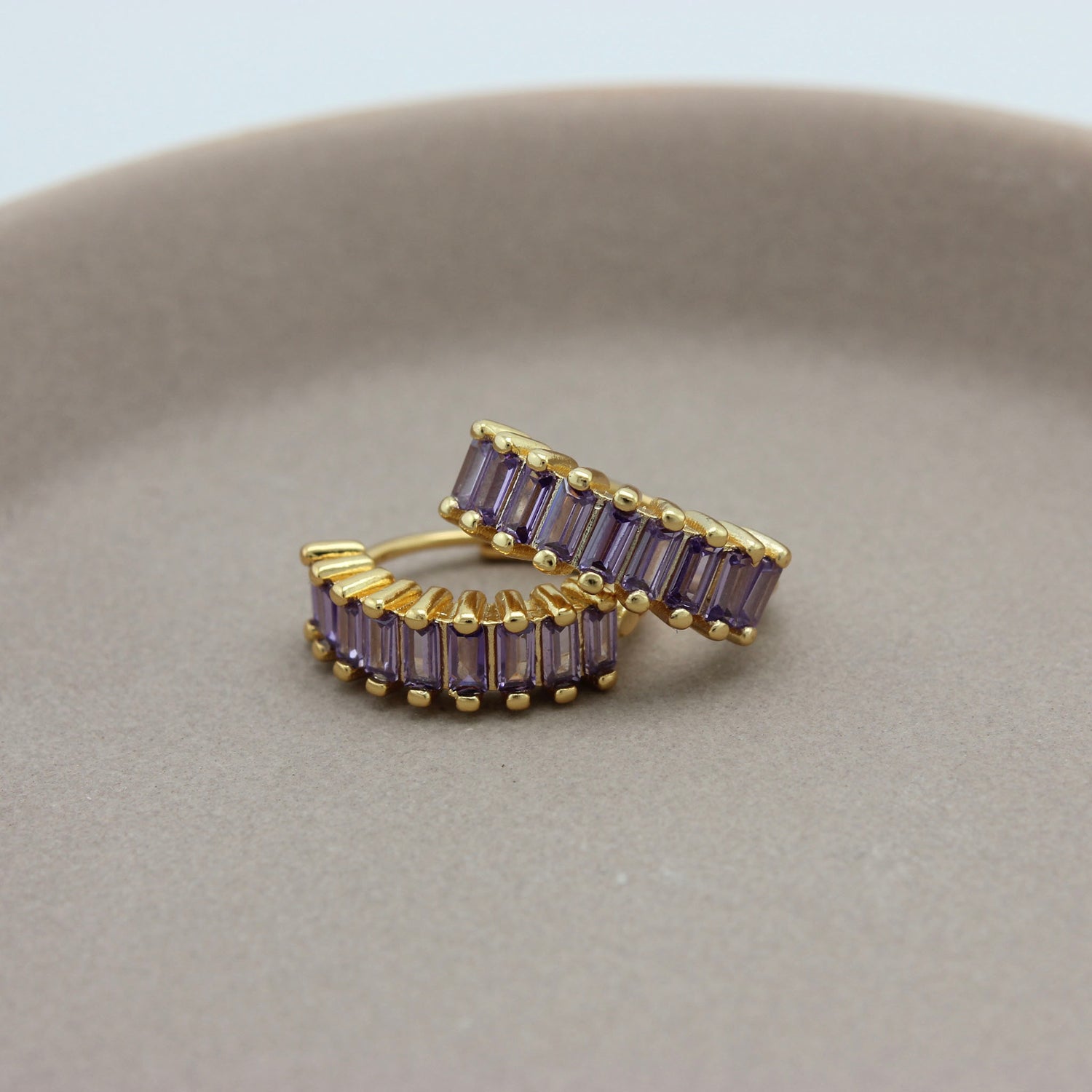 Gouden hoops met paarse zirkonia steentjes liggend op een schaaltje