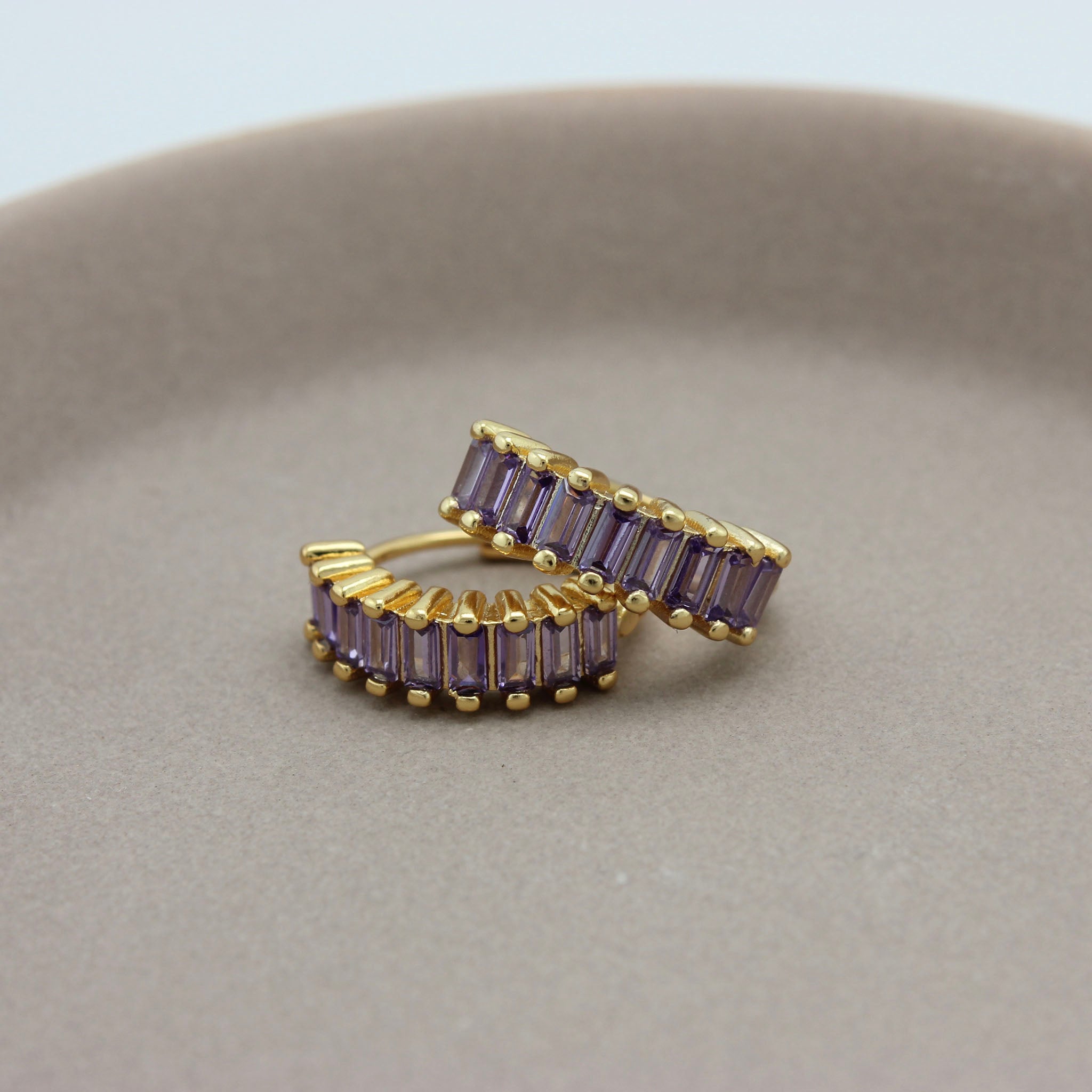 Gouden hoops met paarse zirkonia steentjes liggend op een schaaltje