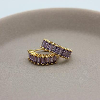 Gouden hoops met paarse zirkonia steentjes liggend op een schaaltje