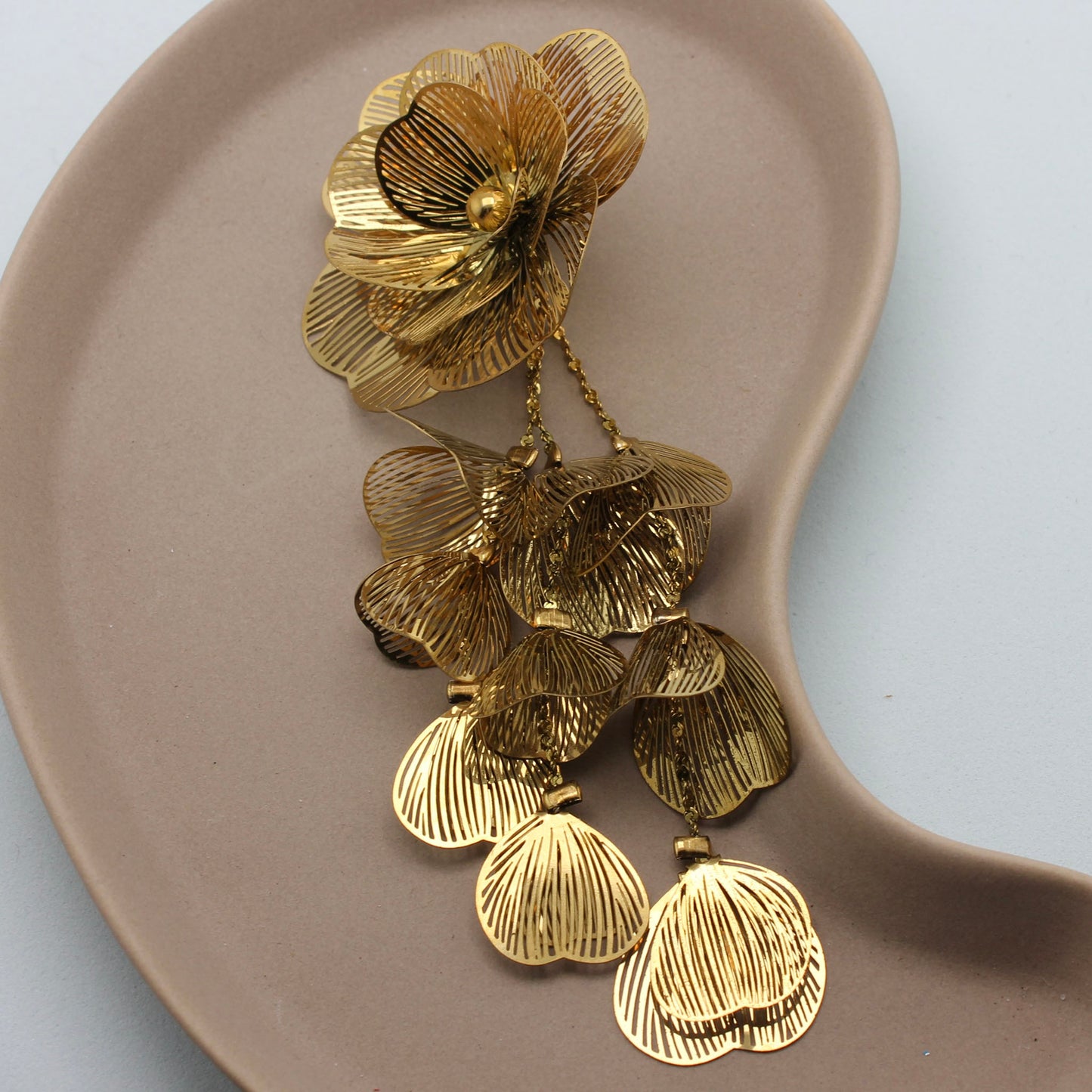 Feestelijke gouden oorbel met hangende bloemen en blaadjes vanuit een zijaanzicht