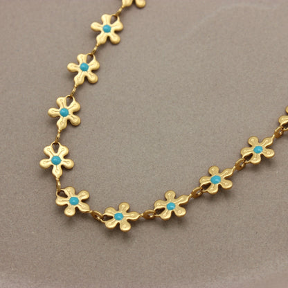 Gedetailleerde foto van een gouden bloemen ketting met een blauwe stip
